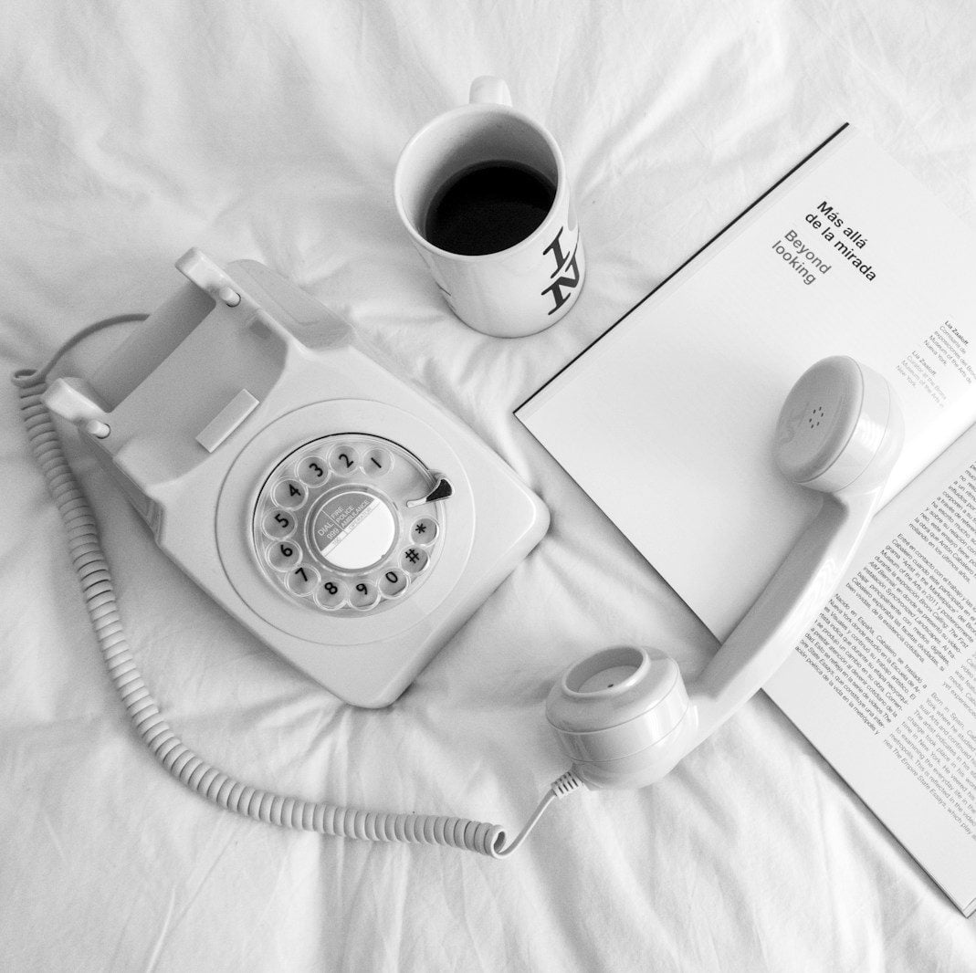 white rotary phone beside white ceramic mug