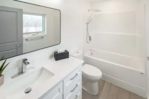 Portfolio 17 Contemporary bathroom in a newly constructed house with a paint job by Trade Grade Painting, showcasing white cabinets, a large mirror, and a bathtub with a modern showerhead.