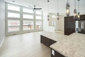 Portfolio 15 Open-concept kitchen and living room in a newly constructed house with a paint job by Trade Grade Painting, showcasing large windows, light wood flooring, modern pendant lighting, dark cabinetry, and a spacious kitchen island.