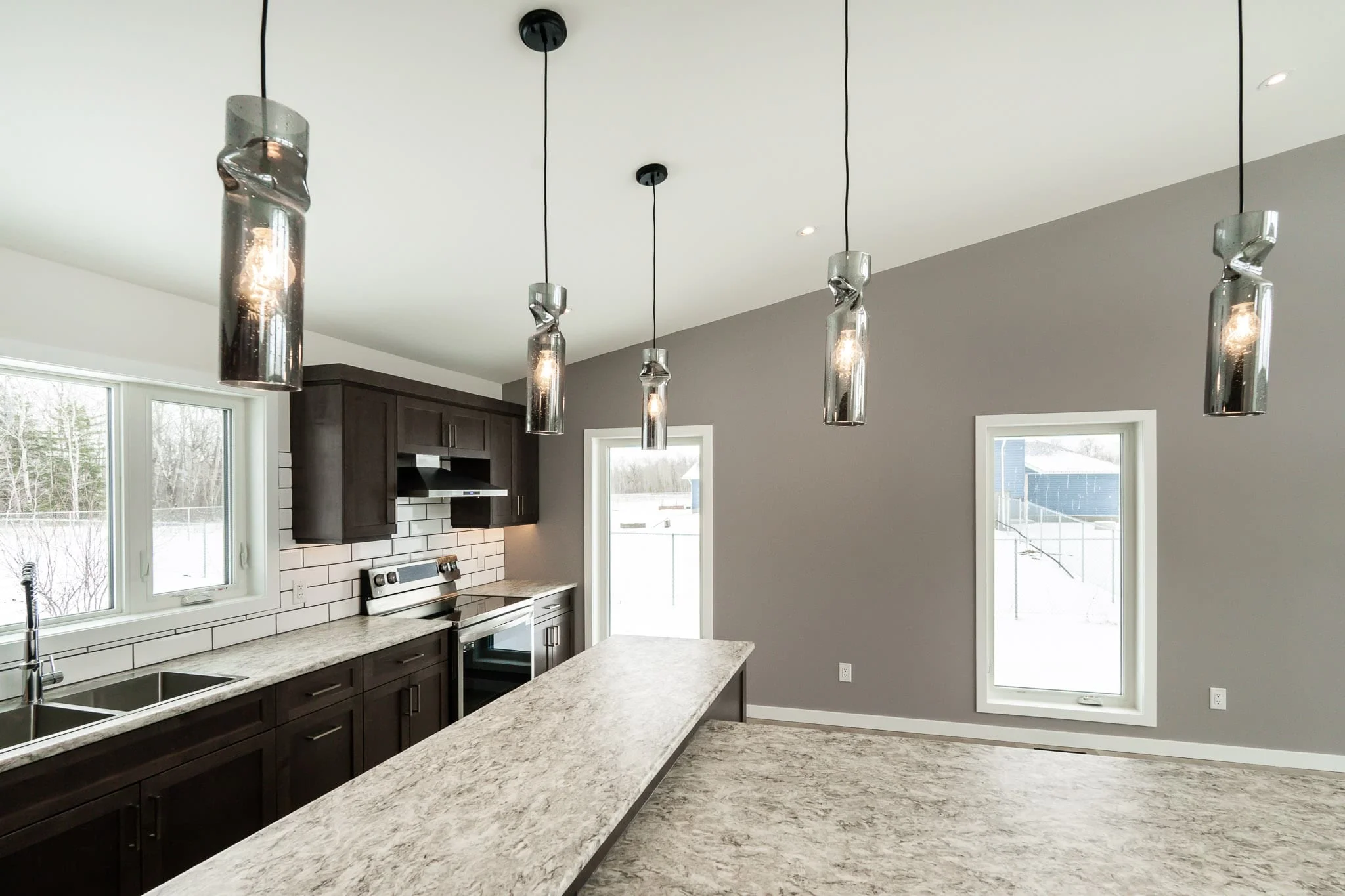 Portfolio 12 Newly constructed house kitchen with a paint job by Trade Grade Painting, featuring modern dark cabinets, light countertops, and unique pendant lighting over the island.
