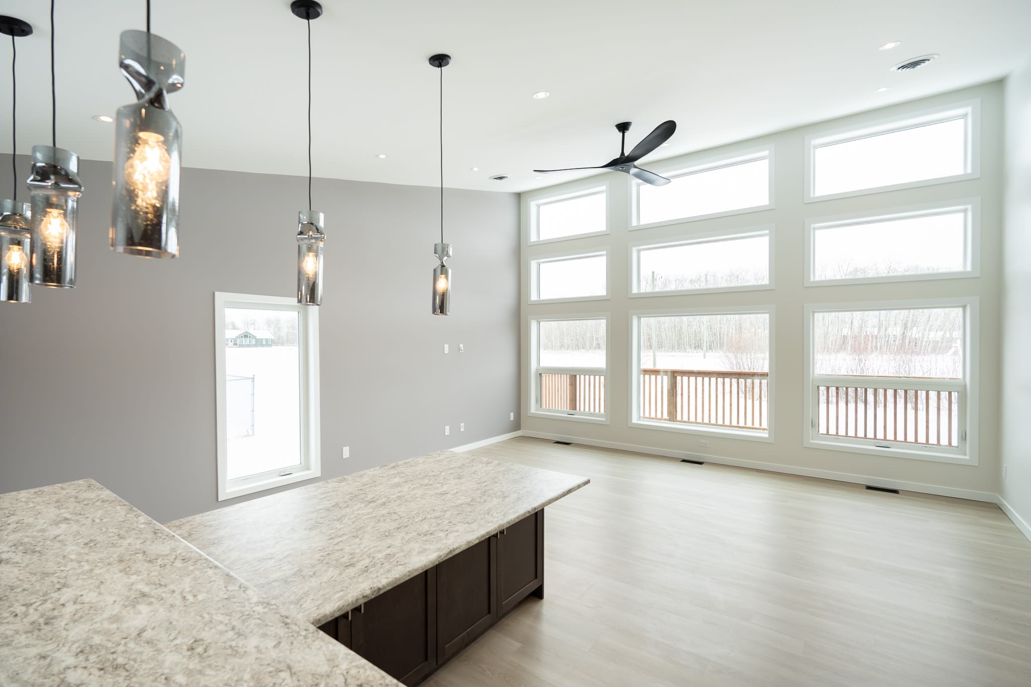 Portfolio 11 Spacious living room in a newly constructed house with a paint job by Trade Grade Painting, featuring large windows, modern pendant lighting, and light wood flooring, creating a bright and airy atmosphere.